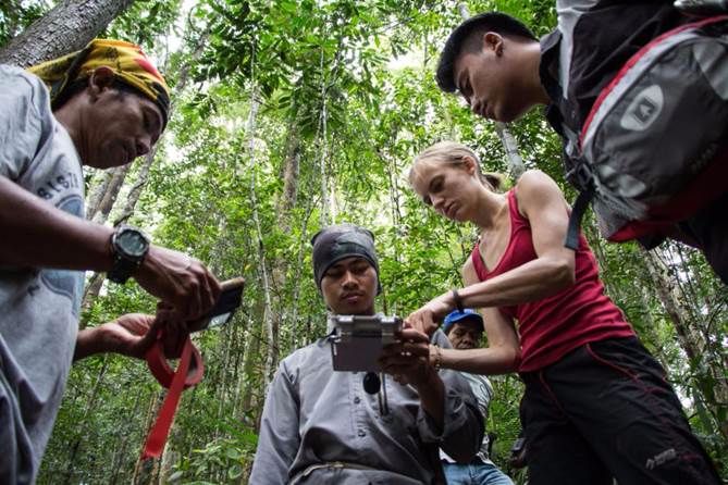 A group of people looking at a device in a forest Description automatically generated