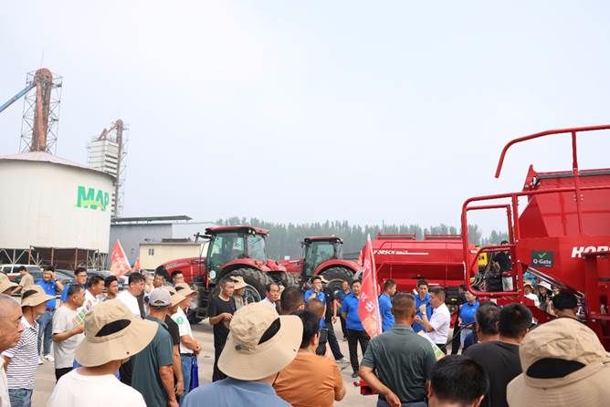 A group of people standing around a red tractor Description automatically generated